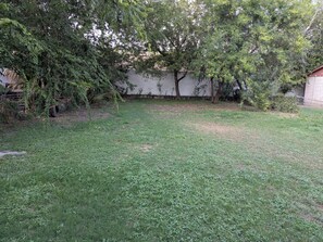 A grassy backyard with trees and a white wall. - Cozy Southtown nearby King Williams home. Nearby Alamodome and Frost Bank Center (San Antonio)