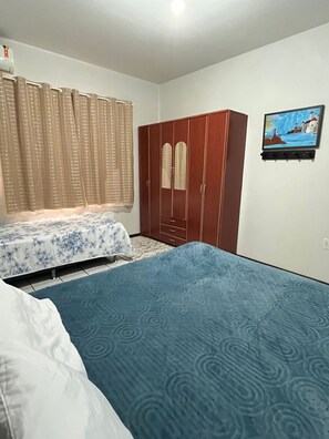 Ein Schlafzimmer mit Bett, Kleiderschrank, einem Fenster mit Vorhängen und einem an der Wand hängenden Bild.
