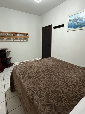 Quarto com cama, escrivaninha, cadeira, porta e quadro na parede.