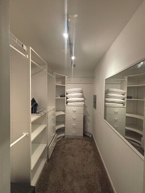 A walk-in closet with open shelving, drawers, and hanging space, featuring a carpeted floor and a ceiling light fixture. -     Cozy 1BR Near Dallas Medical District  - Furnished + Utilities (Dallas)
