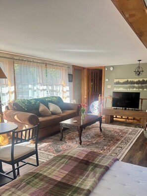 A living room with a sofa, coffee table, TV, and a view of the outdoors. - Peaceful Catskills Getaway - Cozy Studio Loft (Cairo)