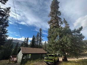 A cabin with a wooden deck and a green pickup truck parked in front. - Charming Alpine Cabin in Alma (Fairplay)