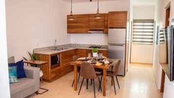Una cocina compacta con armarios de madera, un refrigerador de acero inoxidable y un comedor con una mesa lista para cuatro comensales.