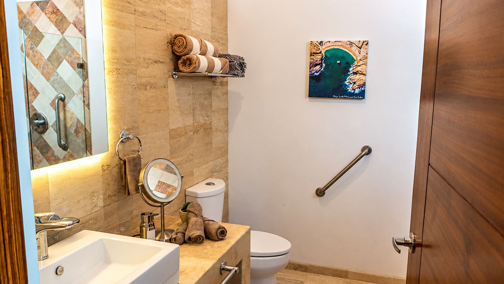 Un baño con lavamanos, espejo, inodoro y toallero con toallas.