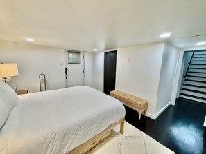 Une chambre à coucher avec un lit, une table de chevet avec une lampe, une porte, un petit banc et un escalier.