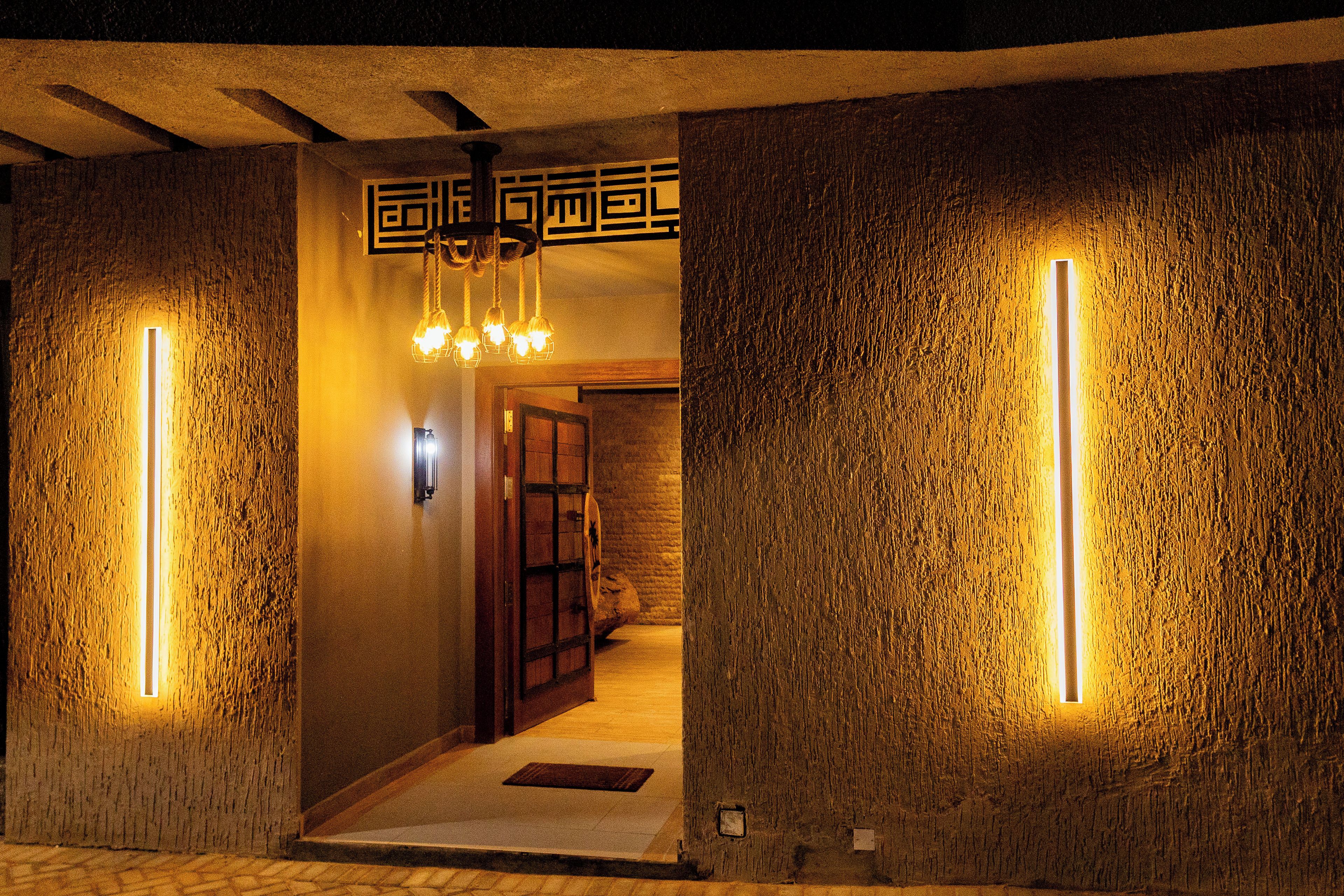 A hallway with textured walls and a wooden door, illuminated by vertical light strips.