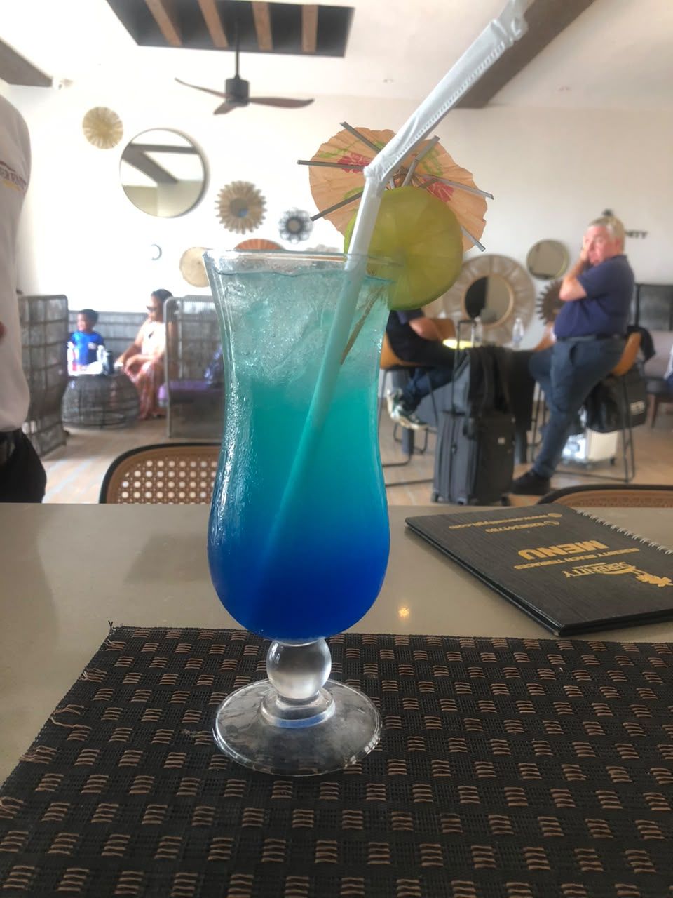 A glass with a blue liquid and a straw, placed on a woven placemat.