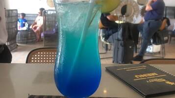 A glass with a blue liquid and a straw, placed on a woven placemat.
