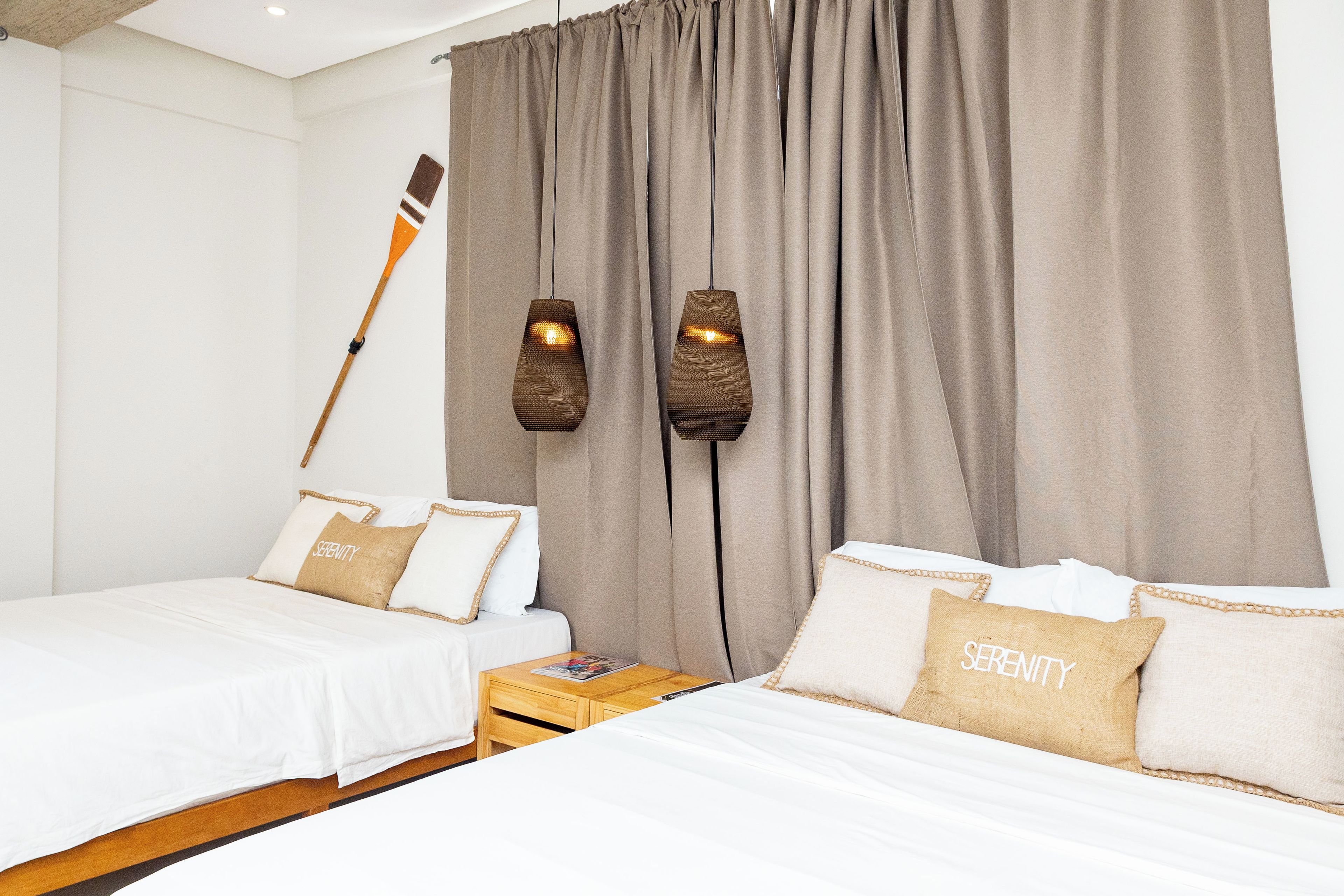 A hotel room with two beds, a wooden nightstand, and two wall-mounted lamps.