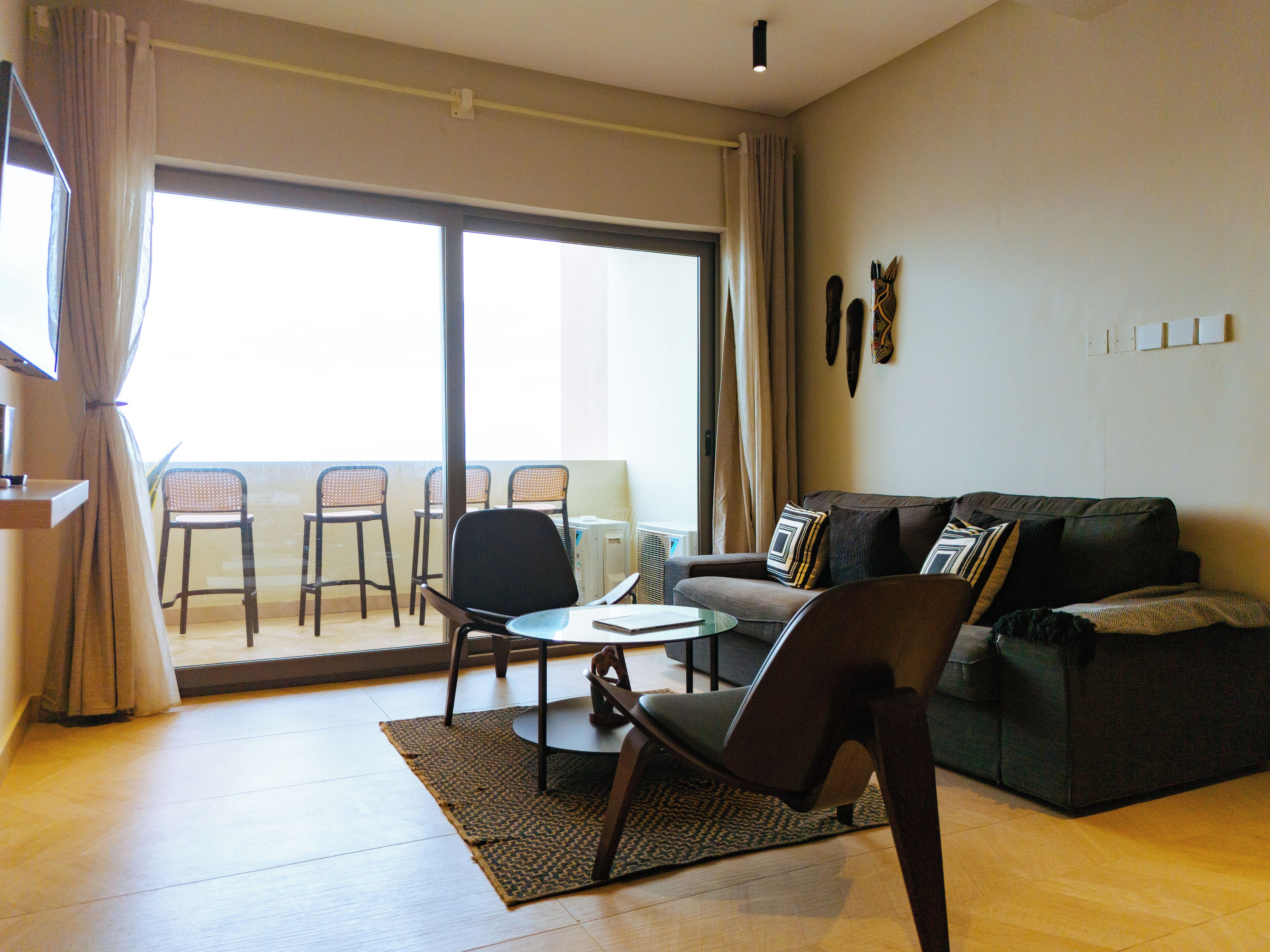 A living room with a sofa, chairs, a coffee table, and a sliding glass door leading to a balcony with chairs.
