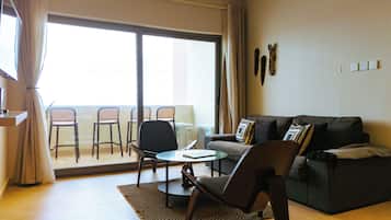 A living room with a sofa, chairs, a coffee table, and a sliding glass door leading to a balcony with chairs.