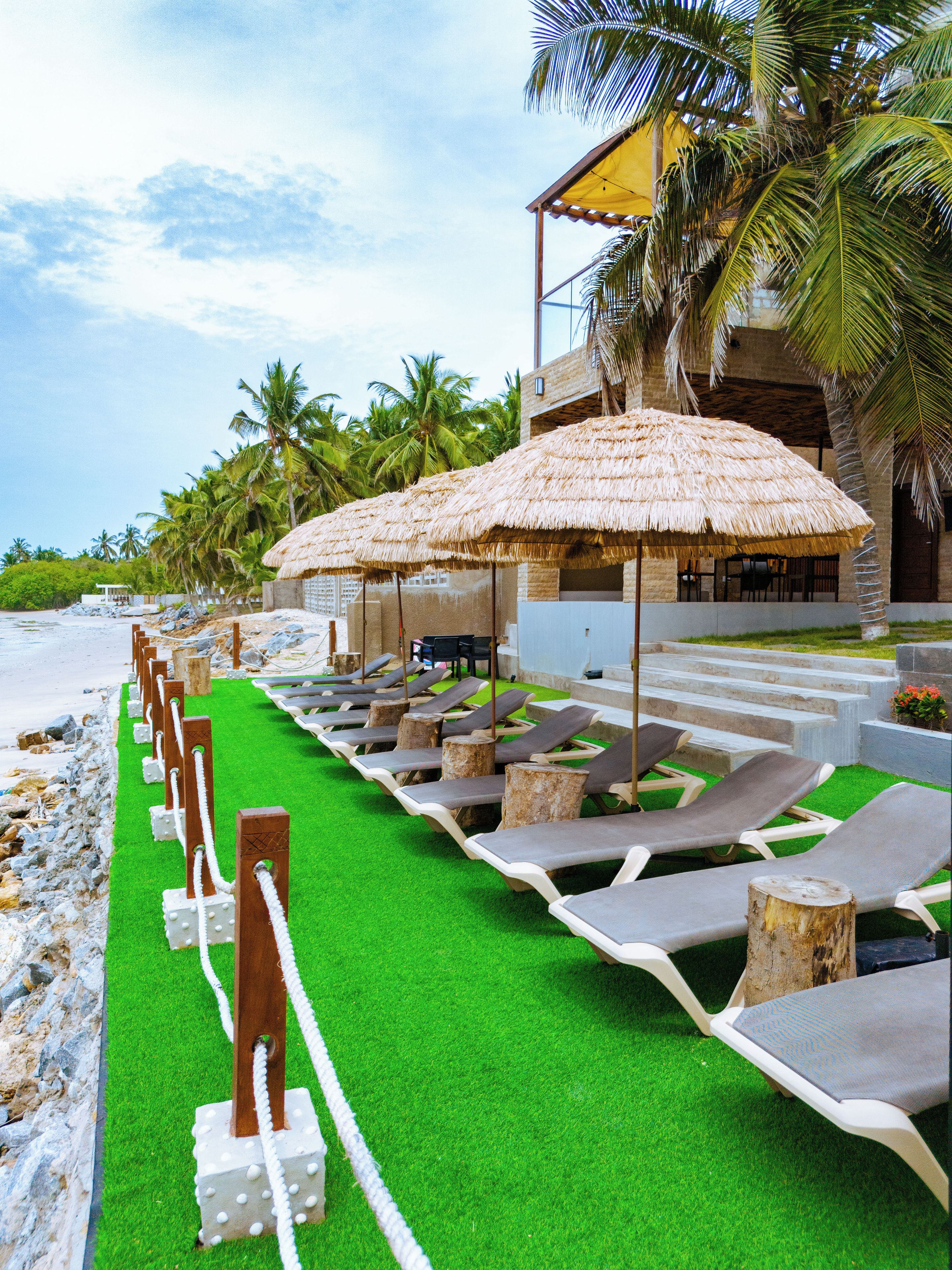 Eine Strandlounge mit Reetdachschirmen, Liegestühlen und einem Pool.