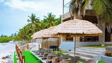 Eine Strandlounge mit Reetdachschirmen, Liegestühlen und einem Pool.