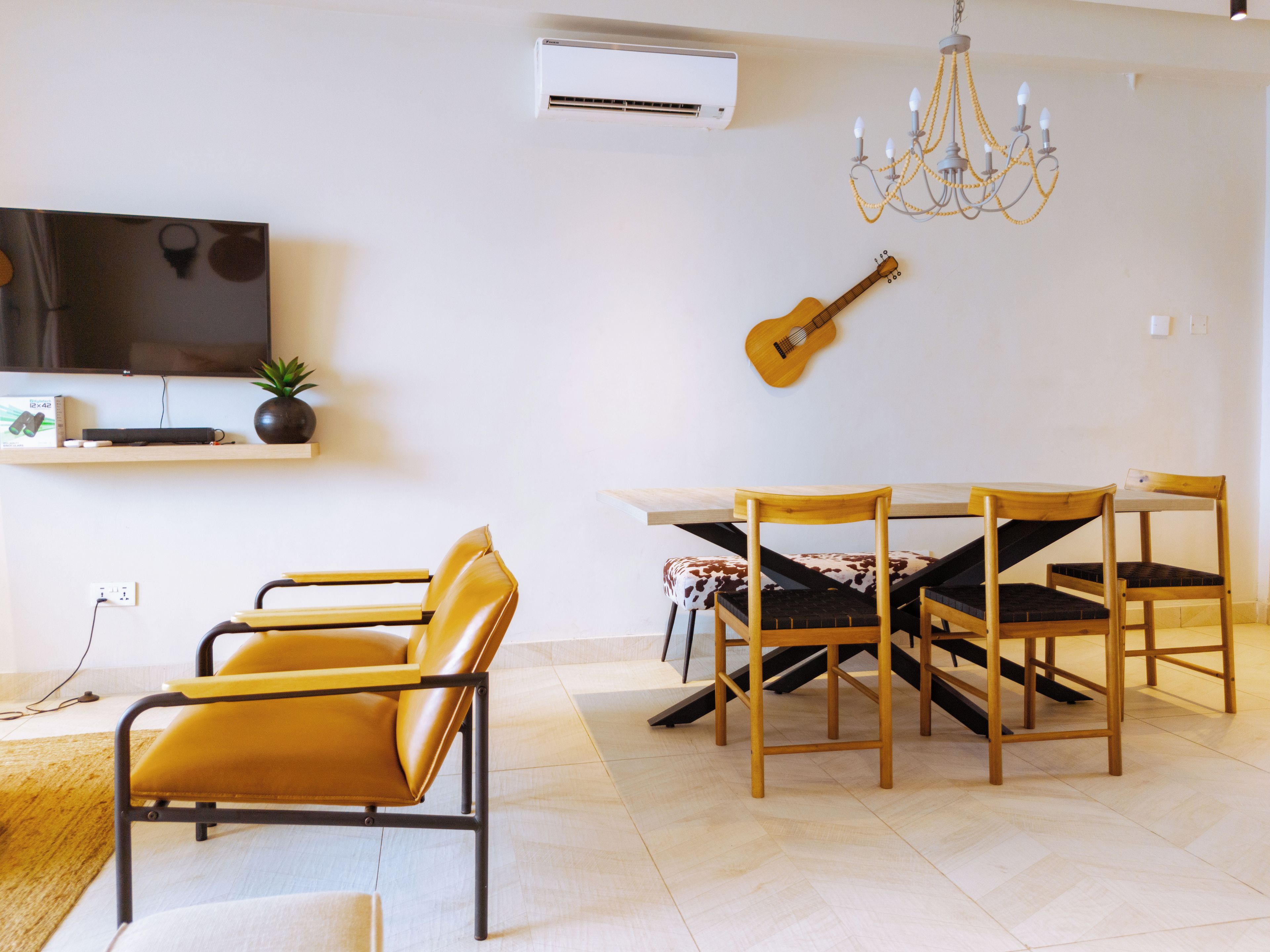 Una sala de estar moderna con televisor, una guitarra, una mesa de comedor con sillas y una araña.