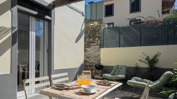 Un espace extérieur aménagé pour les repas, avec une table pour deux, un barbecue et des chaises longues.