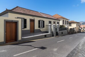 A street view of a residential area with houses featuring tiled roofs and a gated entrance.