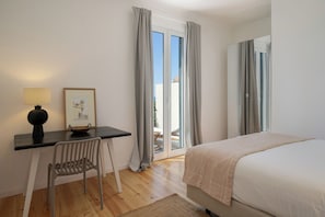 A bedroom with a bed, a desk with a chair, a lamp, and a framed picture.