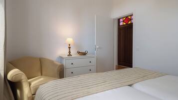 Une chambre à coucher avec un lit, une chaise, une table de chevet avec une lampe et une porte ornée d’un vitrail.
