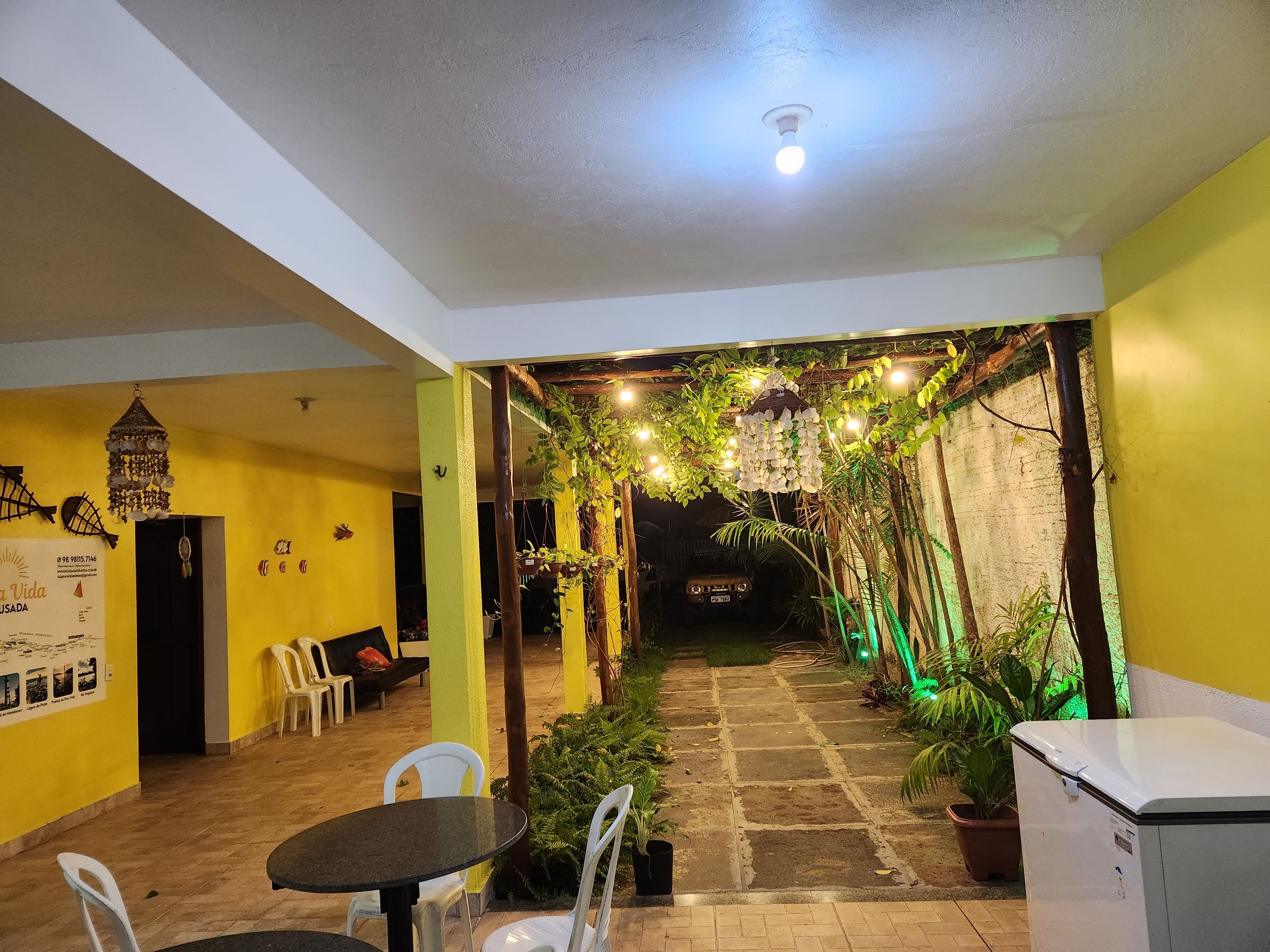 Un patio interior con zona de estar techada, un sendero que lleva a un vehículo y plantas en macetas.