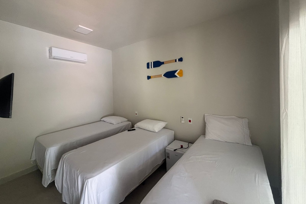 A hotel room with two single beds, a small bedside table with a lamp, and a wall-mounted air conditioning unit.