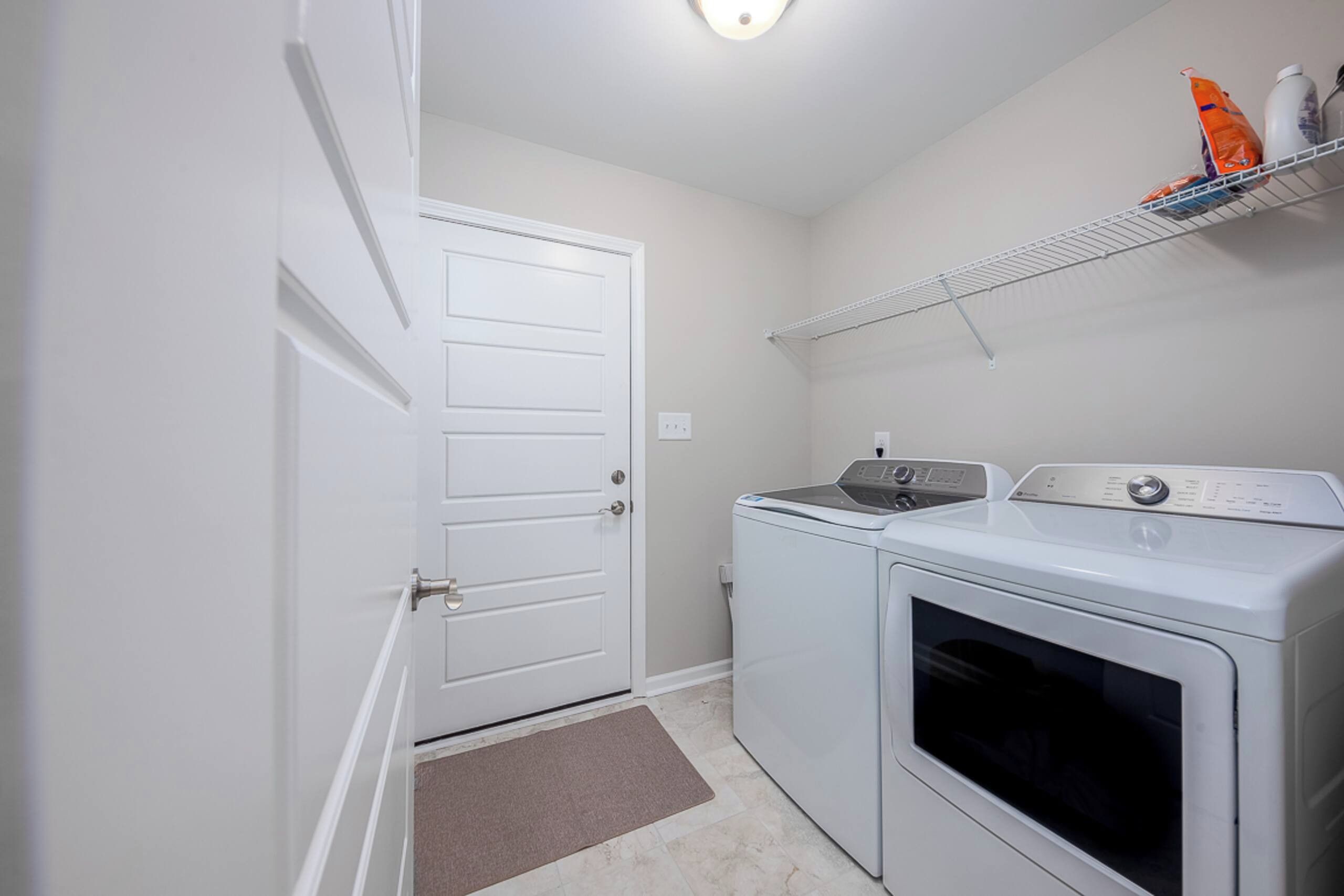 Un cuarto de lavado con una puerta blanca, una lavadora, una secadora y un estante con productos de limpieza.