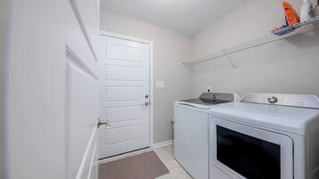Un cuarto de lavado con una puerta blanca, una lavadora, una secadora y un estante con productos de limpieza.