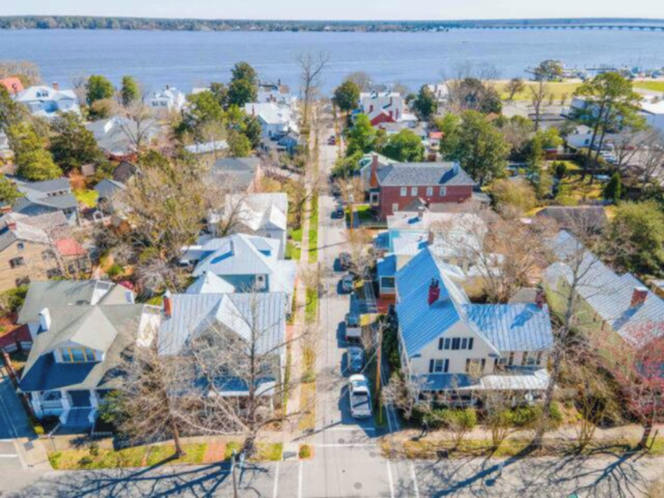 Un quartier résidentiel avec des maisons, des arbres et une étendue d’eau en arrière-plan.