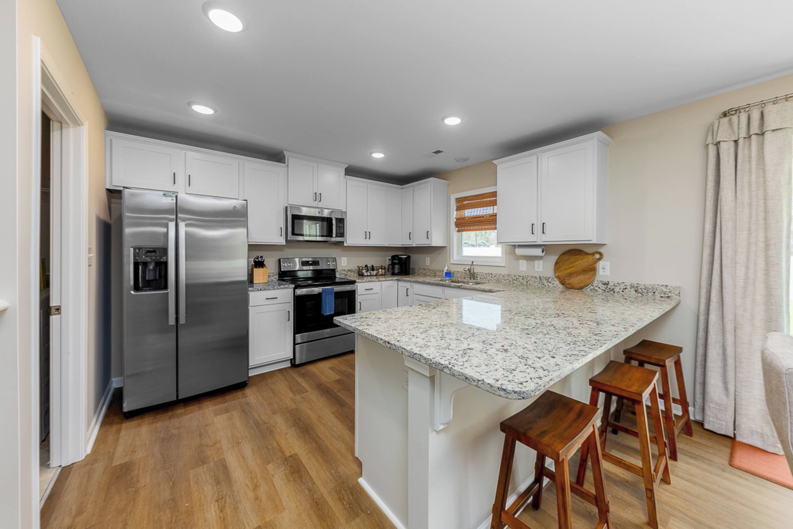 A modern kitchen with stainless steel appliances, white cabinetry, and a granite countertop.