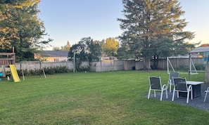 A backyard with a grassy lawn, a wooden fence, and a table with chairs. - Large 5-bedroom Home Near 401.  Ideal for Work Crews & Families. (Cornwall)