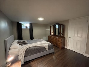 A bedroom with a bed, dresser, mirror, and a window with curtains.