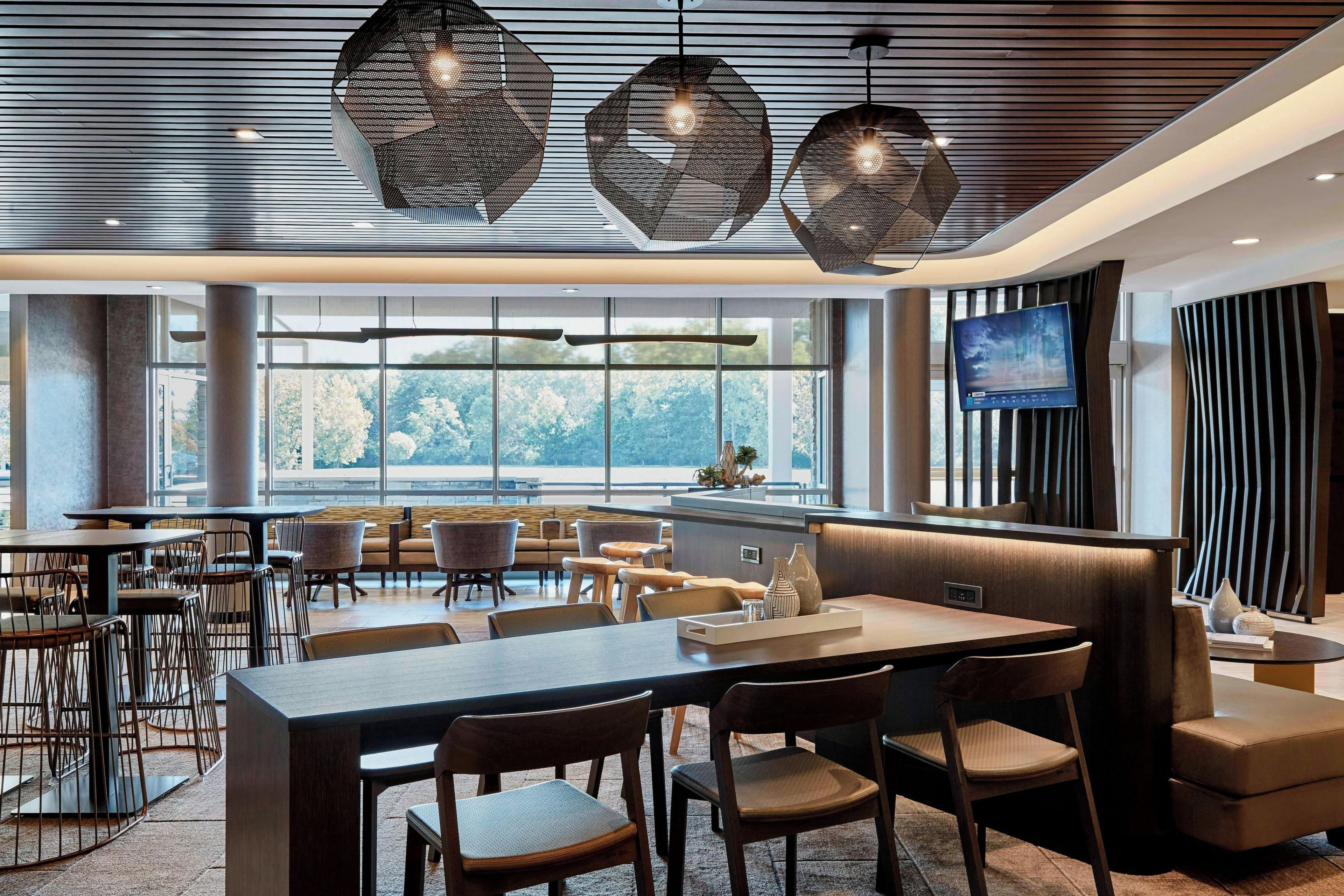 Un comedor moderno con diversas opciones de asientos, incluyendo mesas y cabinas, y grandes ventanales que ofrecen vistas al exterior.