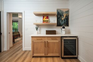 A kitchen with wooden cabinets, a countertop, a Keurig coffee maker, and a painting of a forest. - NEW ! Bear Lake Lodge - Private pond/Hidden speakeasy/pool/pedal boat/kayaks (Broken Bow)
