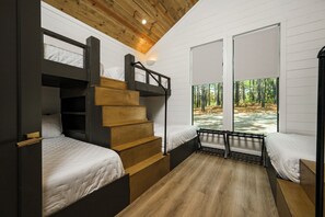 Ein Zimmer mit Etagenbetten, einer Holztreppe und einem Fenster mit Blick auf einen Wald.