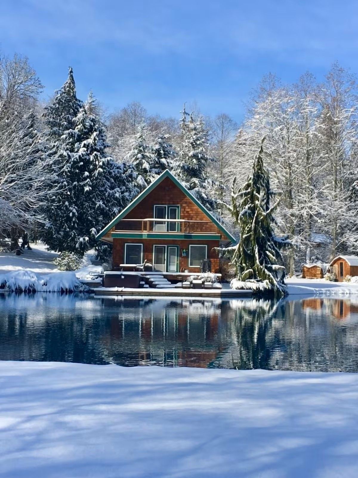 Una baita con un balcone, uno stagno di fronte e alberi coperti di neve.