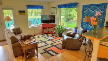 A living room with a sofa, armchair, coffee table, TV stand, and a dining area with a table and chairs.