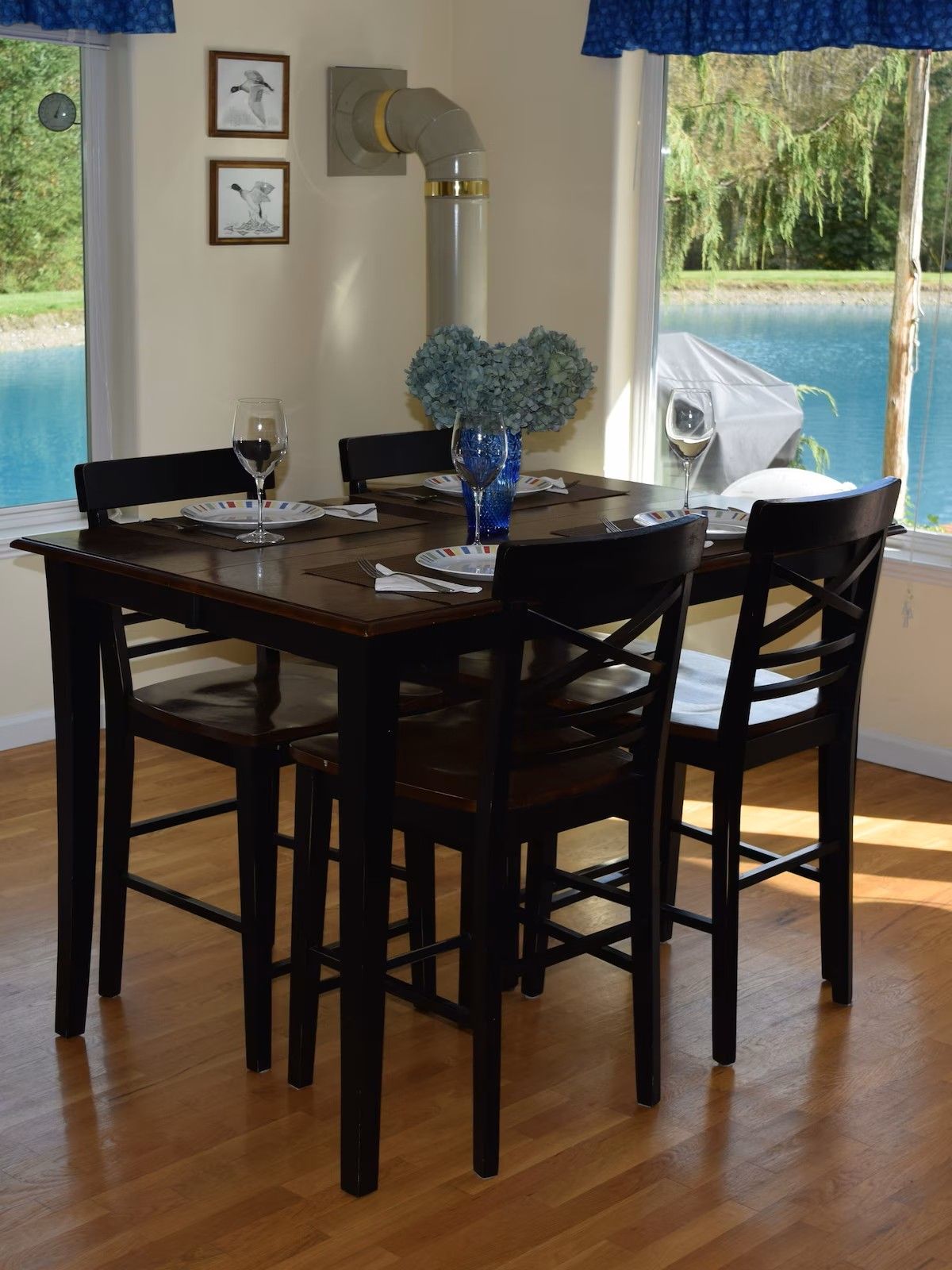A dining table set for four with chairs, a vase of flowers, and a view of a swimming pool.