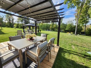 Une terrasse extérieure avec une pergola, une table à manger avec des chaises et un kiosque en arrière-plan.