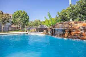 Una piscina con caída de agua, rodeada de una cerca y árboles.