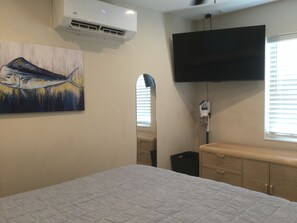 A hotel room with a bed, a painting, an air conditioning unit, a television mounted on the wall, and a window with blinds. - Canal Front, Ocean View, Ice Machine, 60' Prime Dockage! (Marathon)