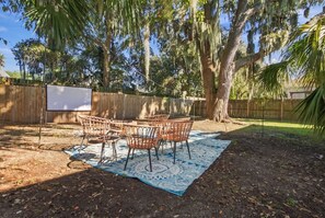 An outdoor seating area with wicker chairs and a blue patterned rug, surrounded by trees and a wooden fence. - 5BR , Sleeps 14 , Central to Downtown & Tybee (Savannah)