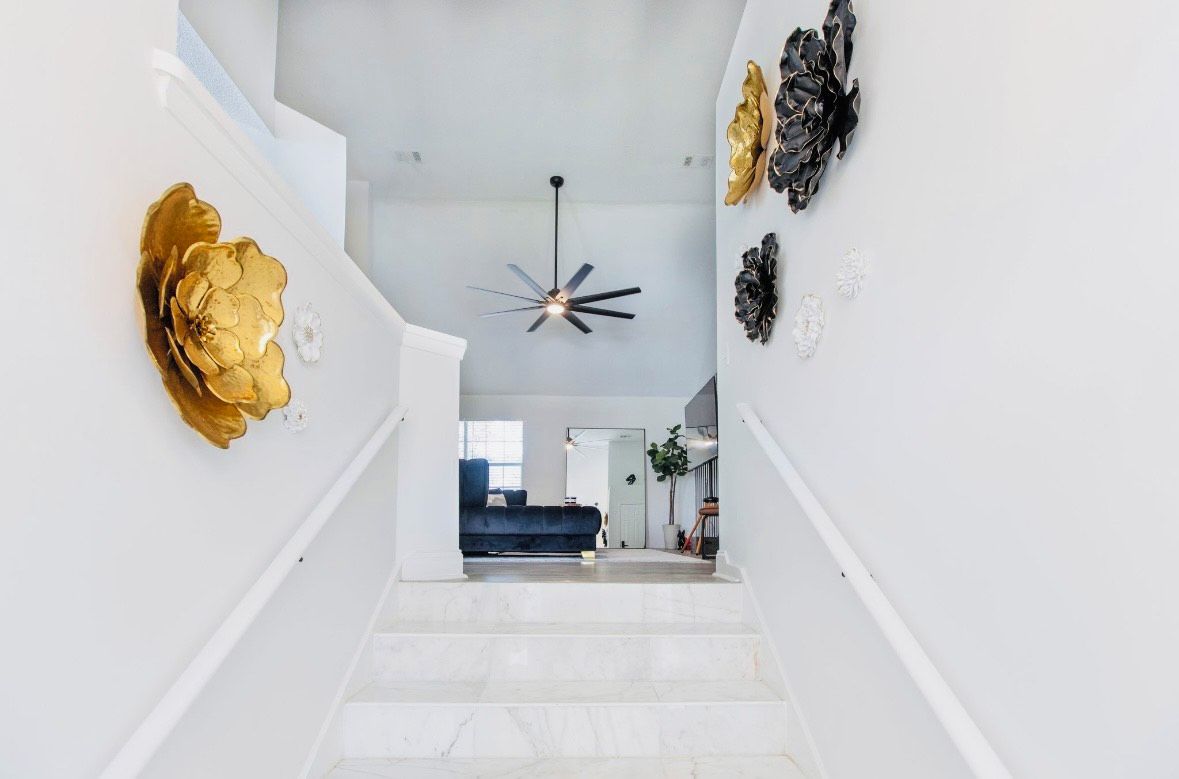 Una escalera conduce a una sala de estar con ventilador de techo y decoración mural.