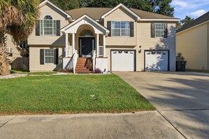 A two-story house with a front porch, a garage, and a well-maintained lawn. - 5BR , Sleeps 14 , Central to Downtown & Tybee (Savannah)