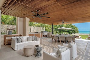 Un patio exterior con techo de madera, ventiladores de techo, una mesa de comedor con sillas, un sofá y una parrilla.