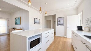 Une cuisine moderne avec des meubles blancs, un four à micro-ondes encastré et des luminaires suspendus.