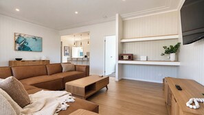 Un salon moderne avec un canapé en cuir marron, une table basse en bois et un téléviseur posé sur une étagère fixée au mur.