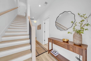 A staircase with wooden steps leading to a landing, a console table with a vase and a bowl, and a wall-mounted mirror. - Nashville Hideaway | Amazing Rooftop Patio & Views (Nashville)