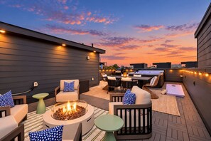 An outdoor patio with seating, a fire pit, and string lights against a sunset sky. - Nashville Hideaway | Amazing Rooftop Patio & Views (Nashville)
