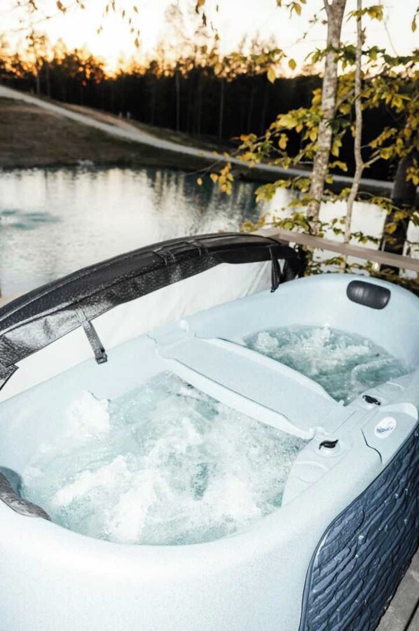 A hot tub with a view of a body of water and trees in the background. - Twilight at Lux in the Gorge - Hot Tub - Fishing - Shared Pond with Kayaking, Swimming, & Pedal Boat - Game Room with Pool Table, Foosball, Ping Pong, Air Hockey, and More! (Campton)