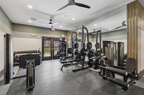 Un gimnasio con diferentes equipos de ejercicio, un ventilador de techo y una puerta que da al exterior.