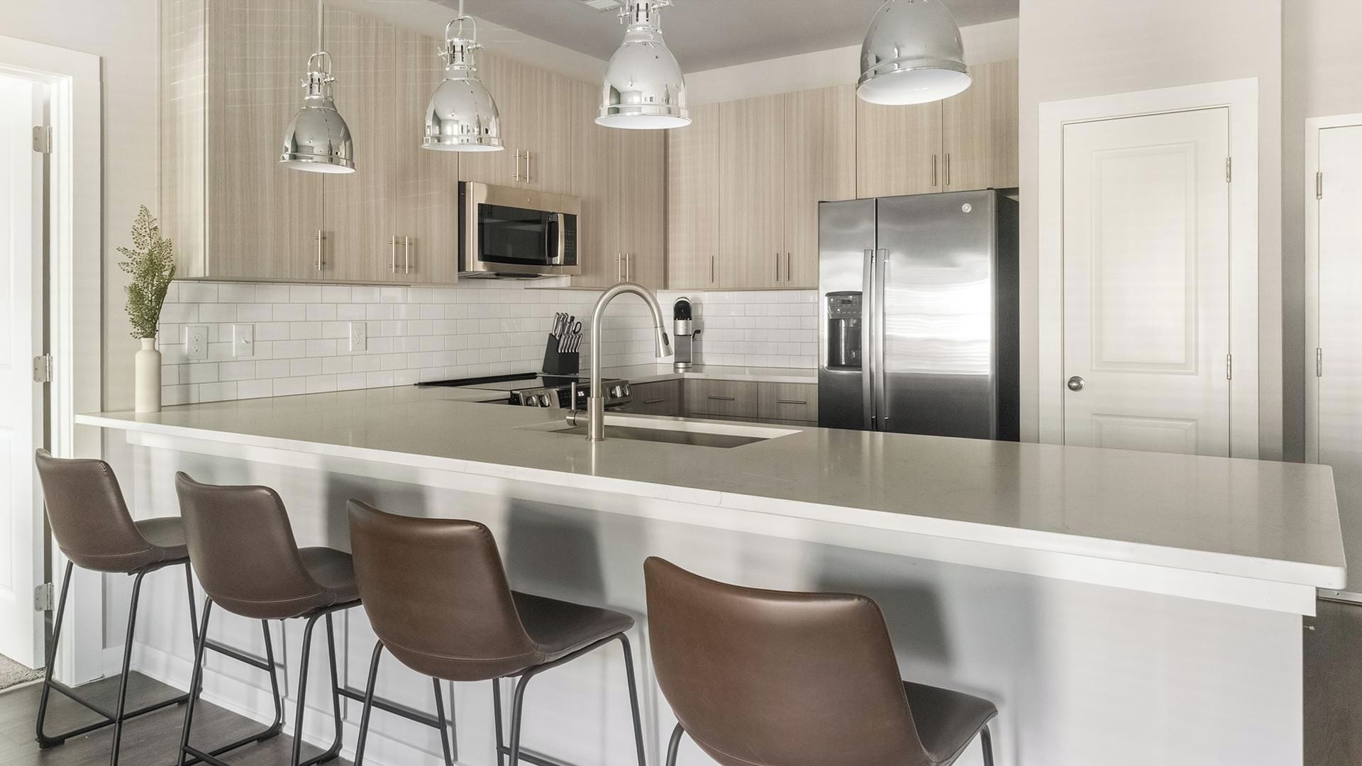 A modern kitchen with a large island, stainless steel appliances, and pendant lighting.
